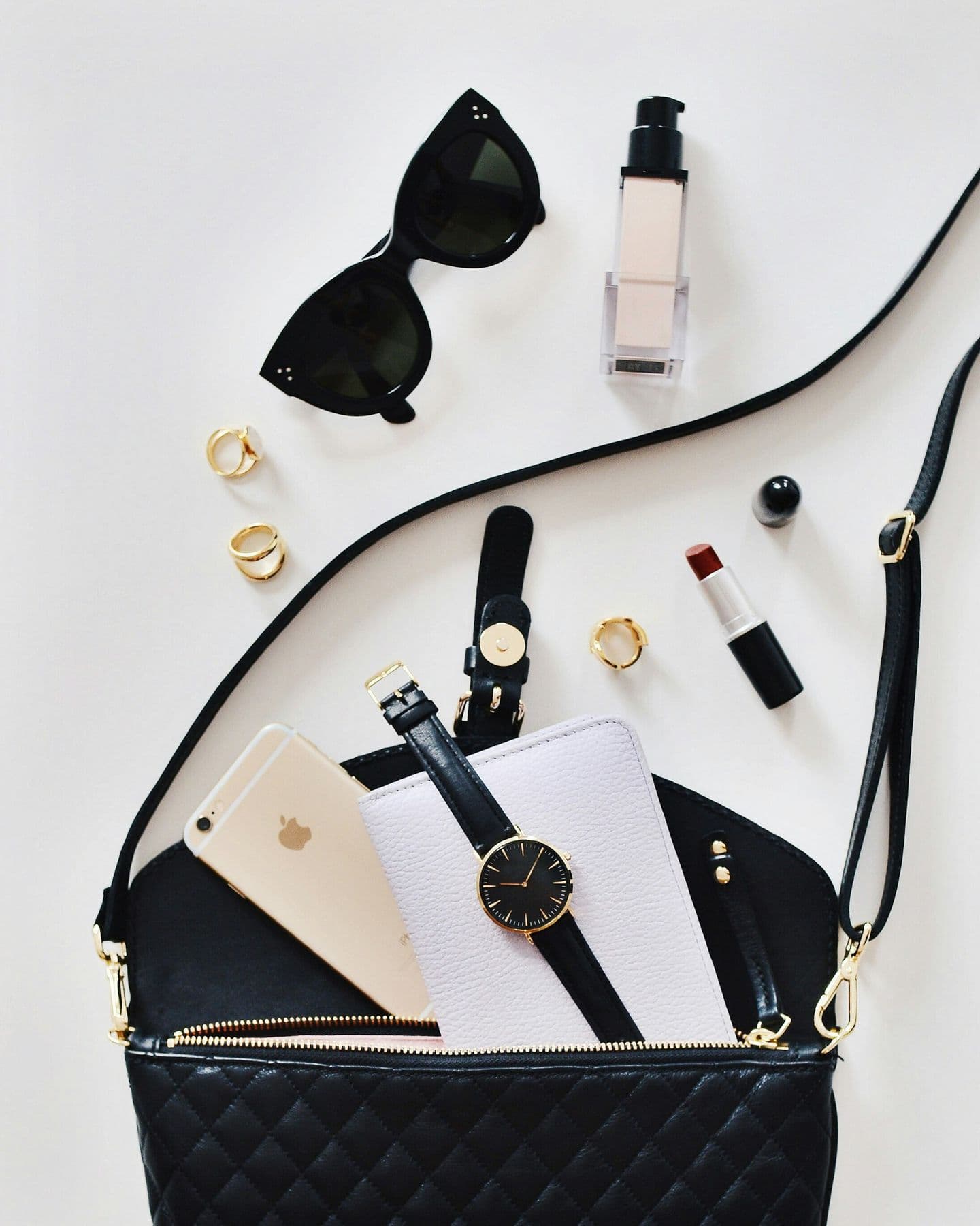 Flat lay of a quilted black bag, sunglasses, a watch and beauty products