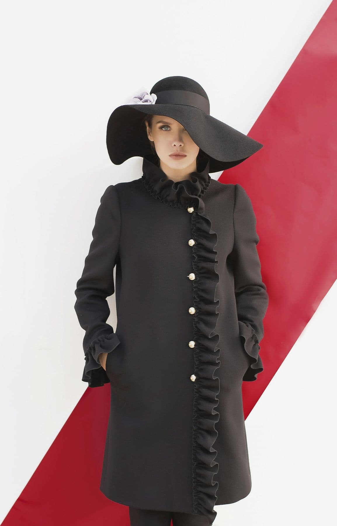 Woman in a black coat and wide-brim hat against a red diagonal