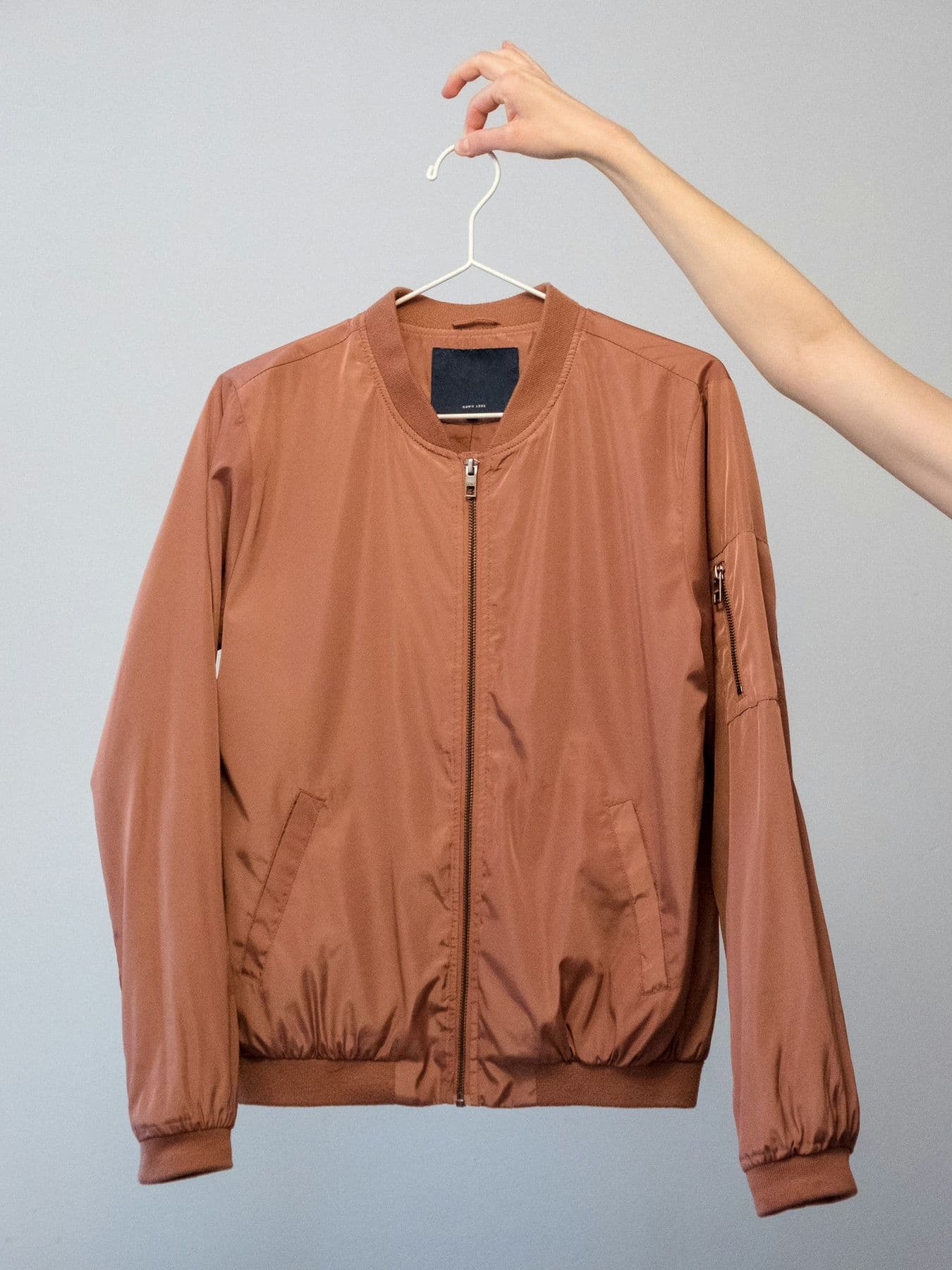 Rust bomber jacket held up on a hanger