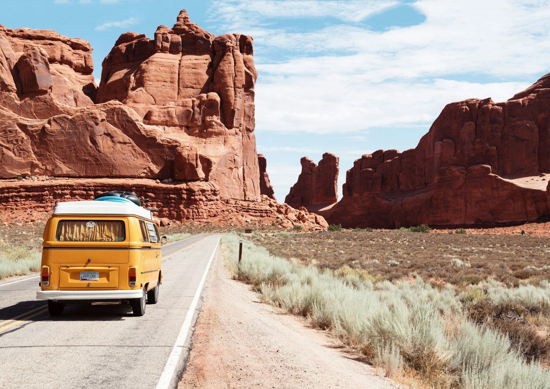 Vintage yellow camper van on a desert road among red rock formations