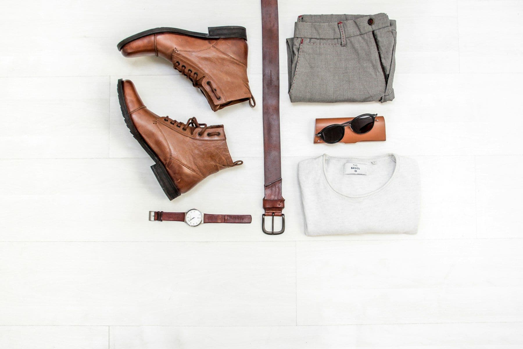 Flat lay of brown leather boots, folded trousers, a belt and sunglasses