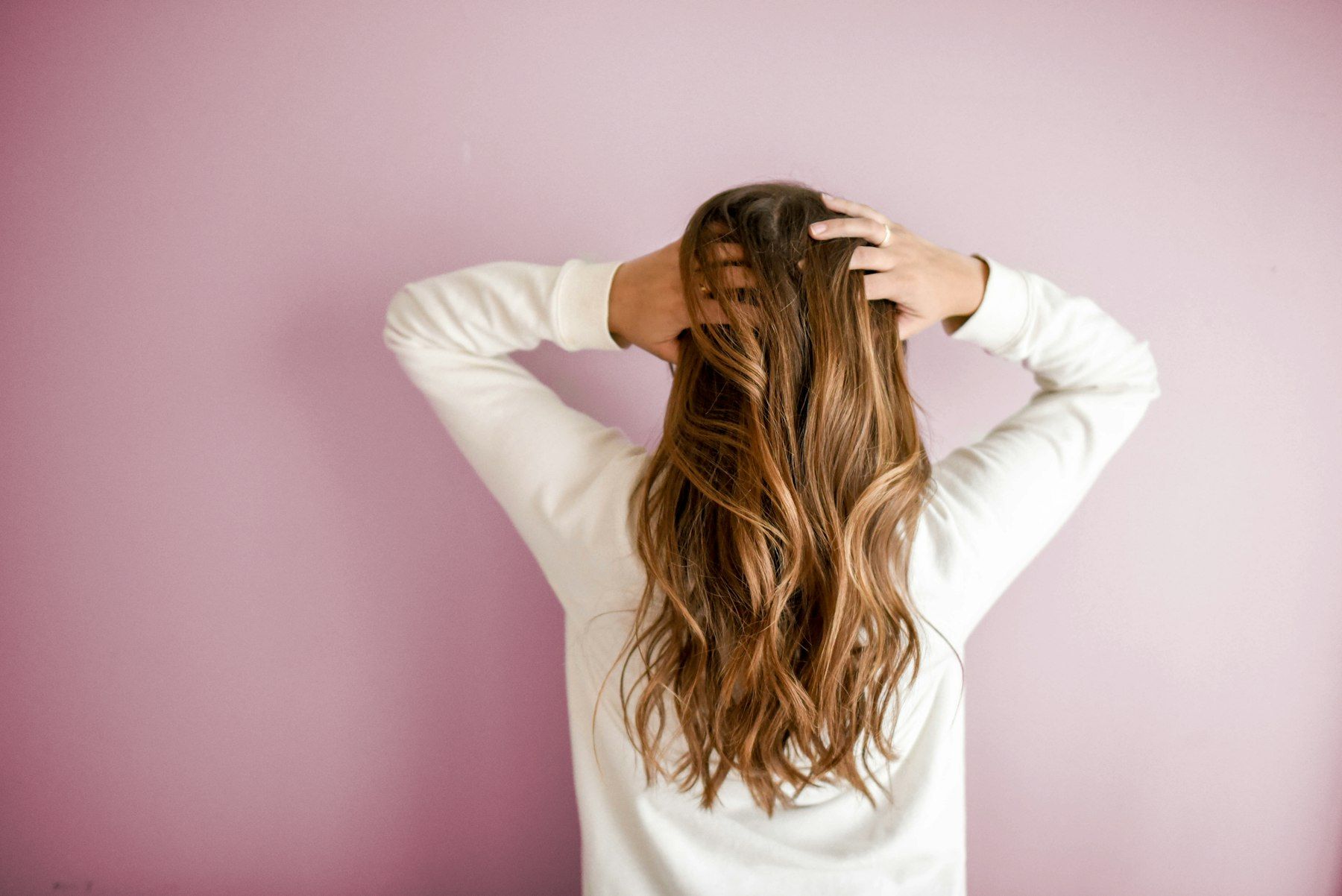 Woman with long wavy hair seen from behind against a pink wall