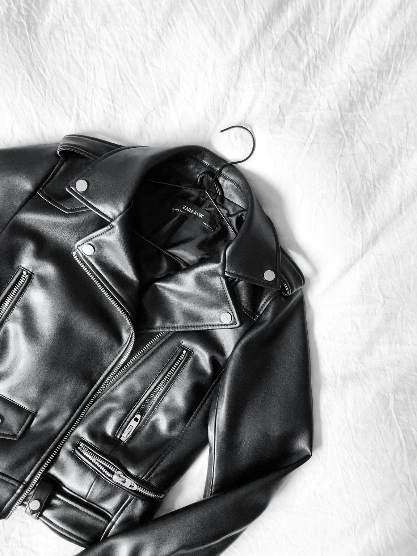 Black leather biker jacket on a hanger against white sheets