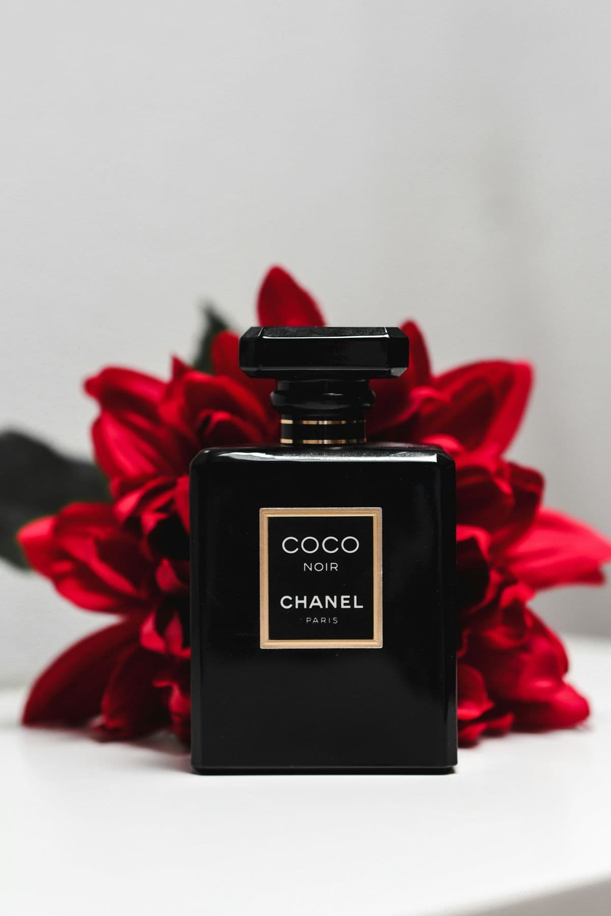 Black perfume bottle in front of red flowers