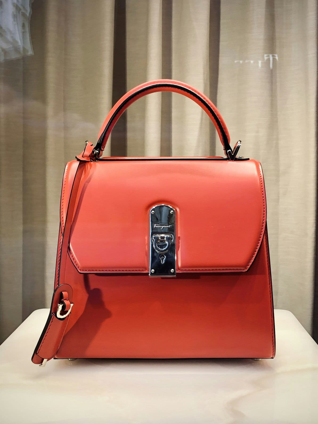 Structured red top-handle bag on a pedestal