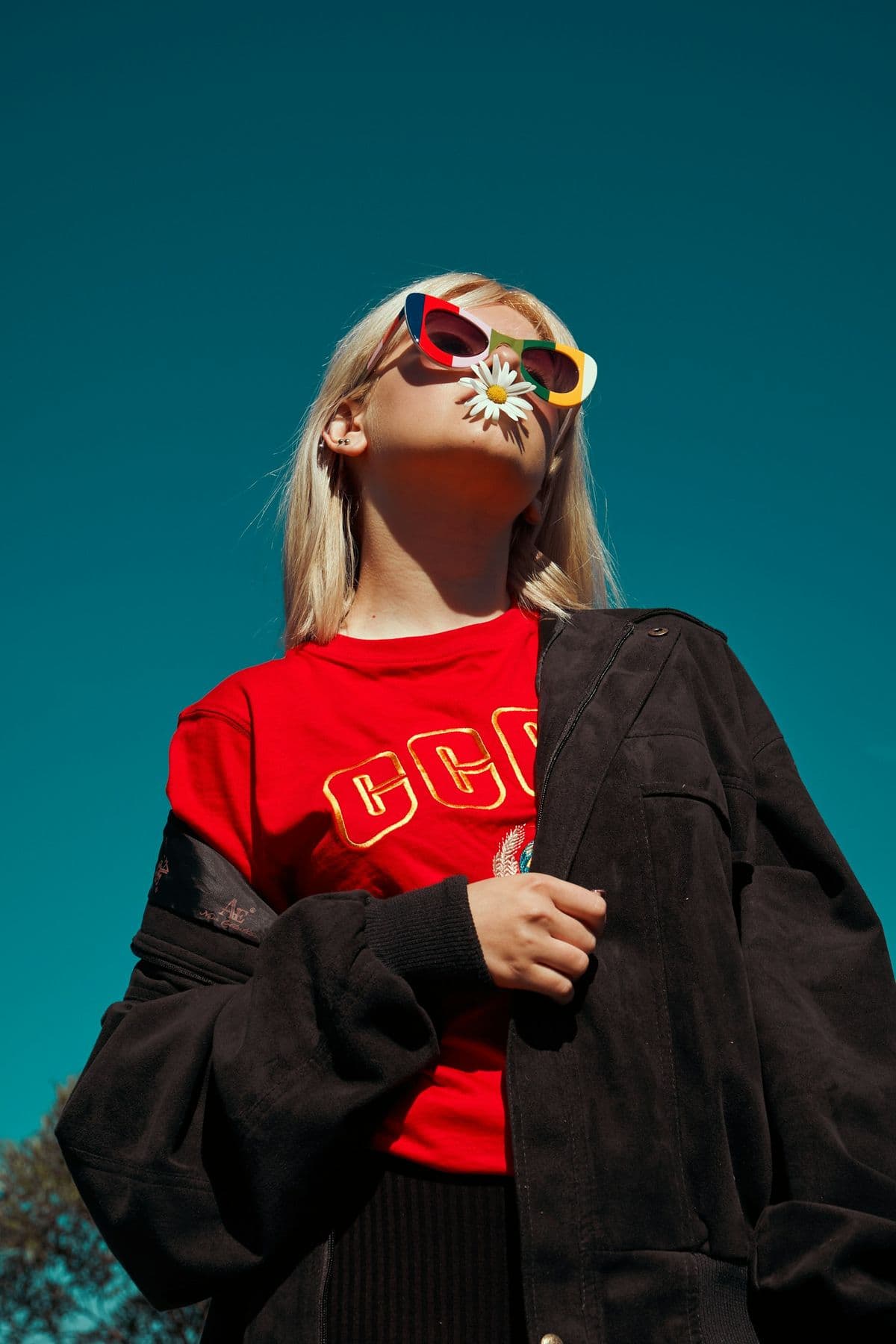 Woman in a red sweater and oversized black coat against a teal sky