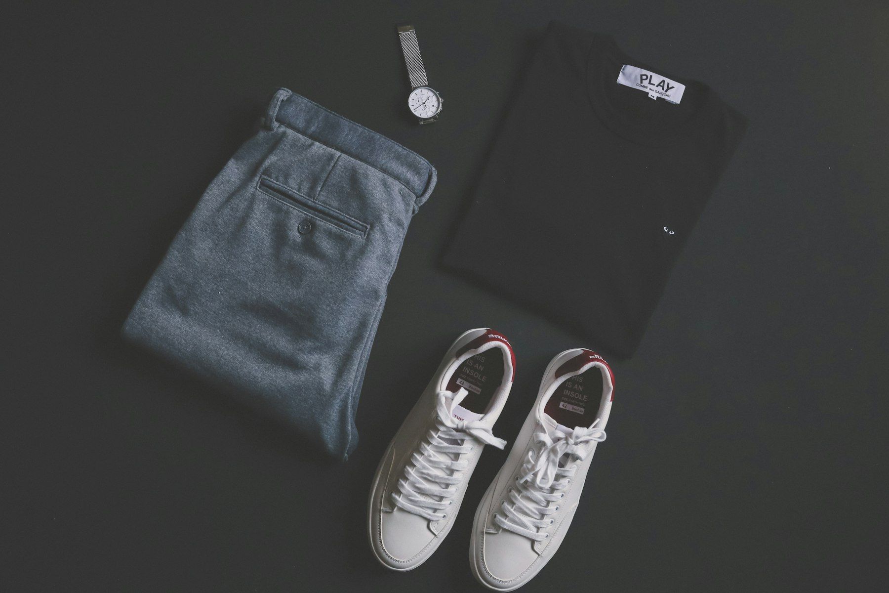 Flat lay of white sneakers, chinos, a black tee and a watch