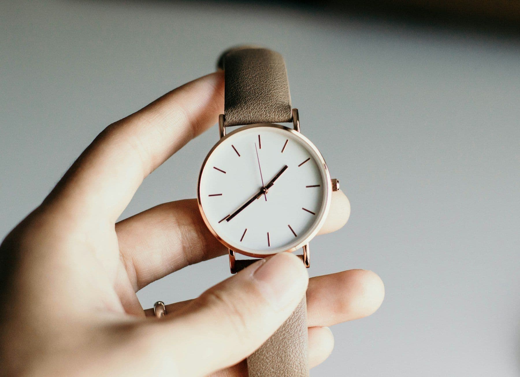 Hand holding a minimal watch with a brown strap