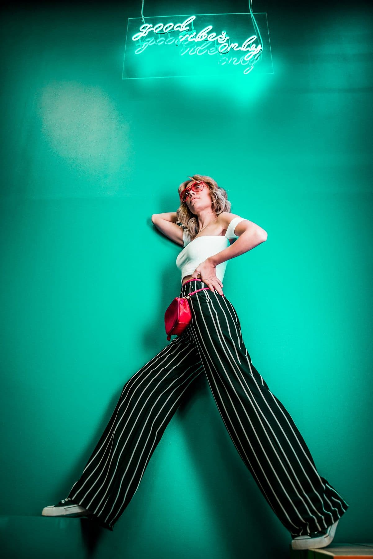 Woman in striped wide-leg trousers beneath a neon sign on a green wall