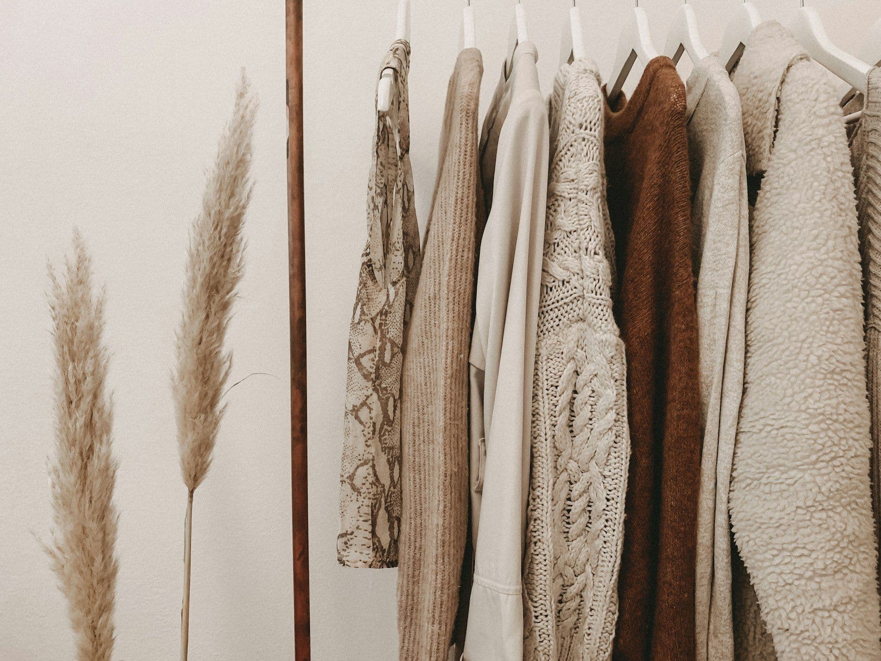 Rail of oatmeal knits beside dried pampas grass
