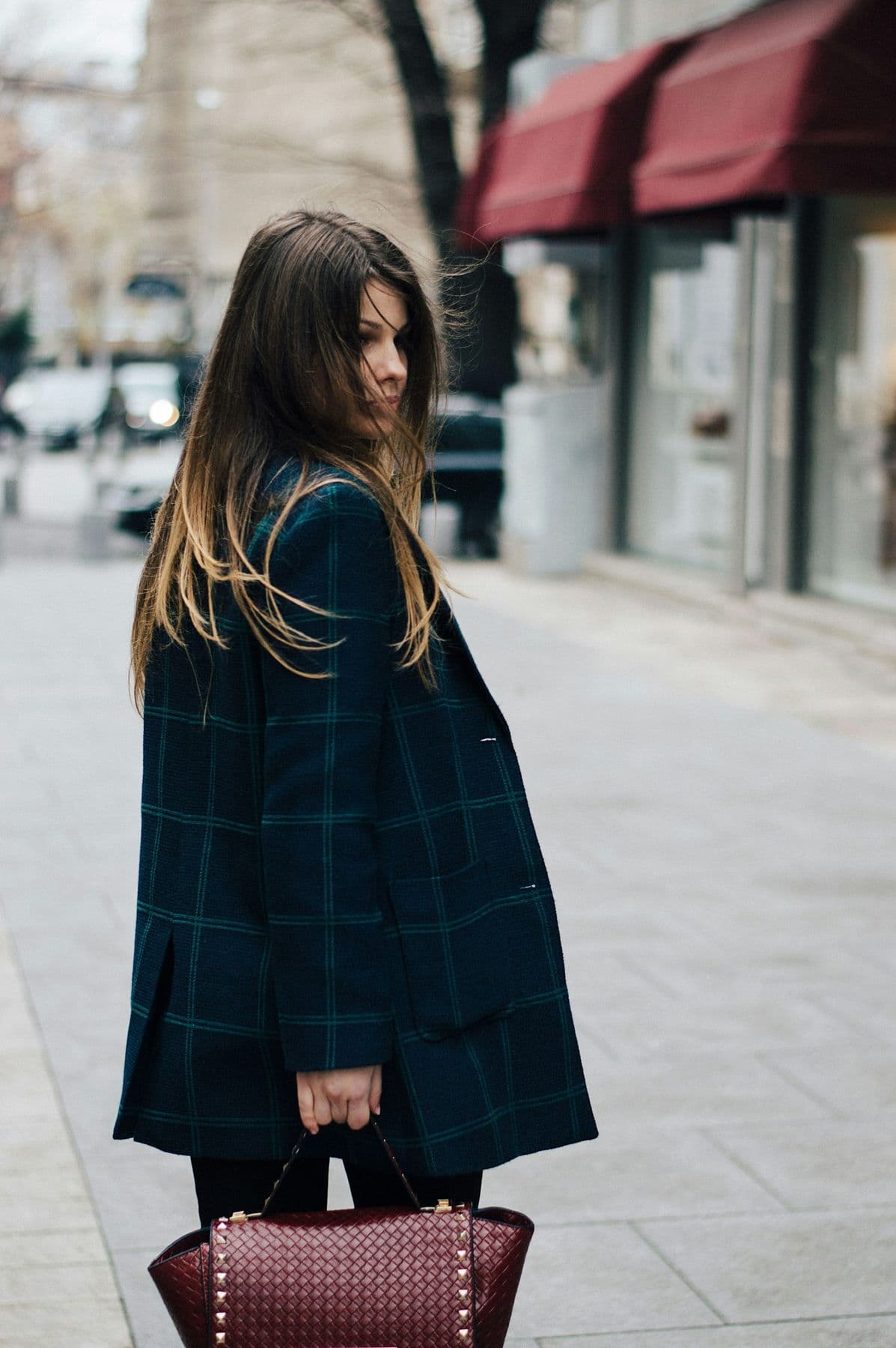 Woman in a tartan coat carrying a studded bag on a city street